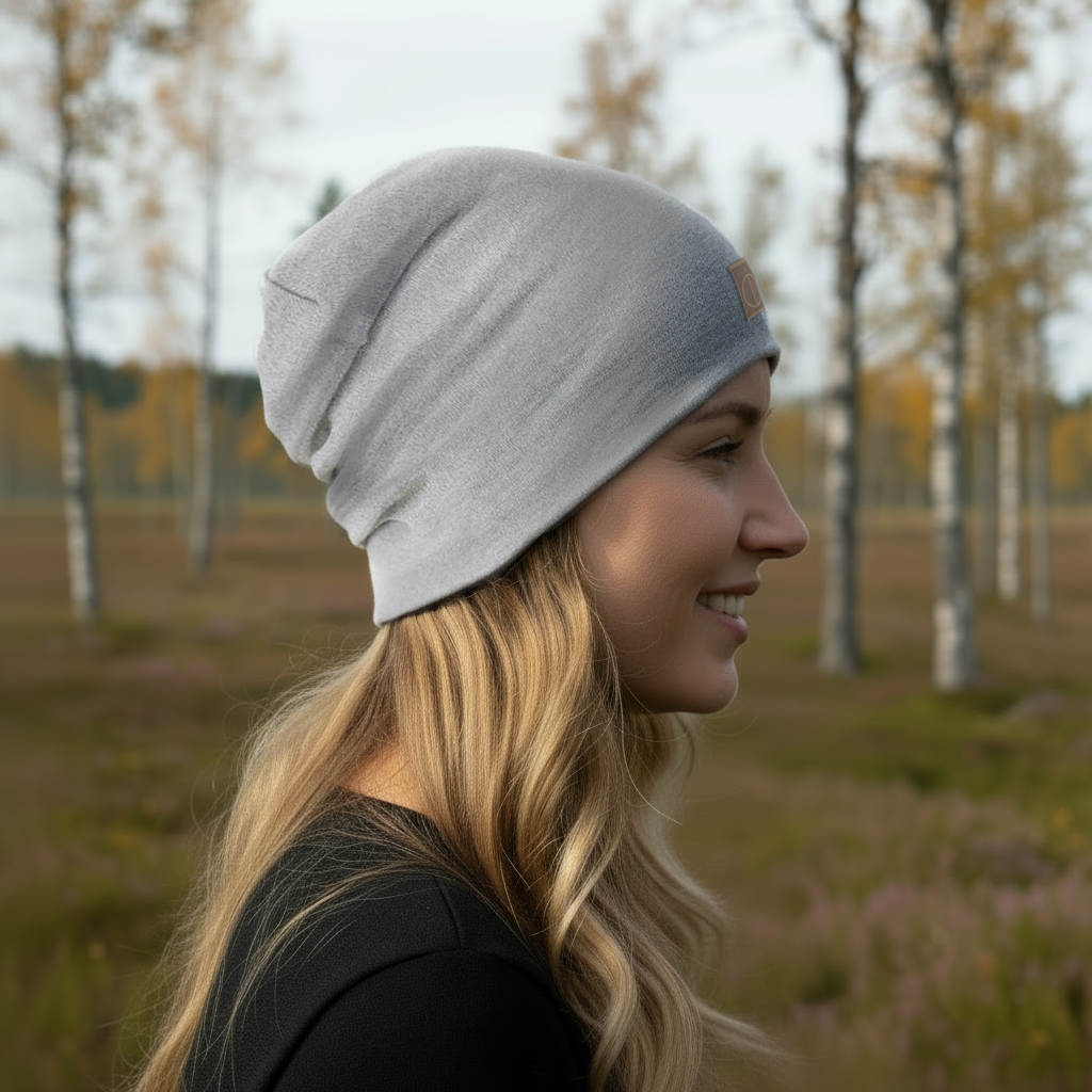 Vaaleanharmaa merinovillapipo naisen päässä sivuprofiilissa syksyisessä maisemassa. Damaski, merinovilla.
