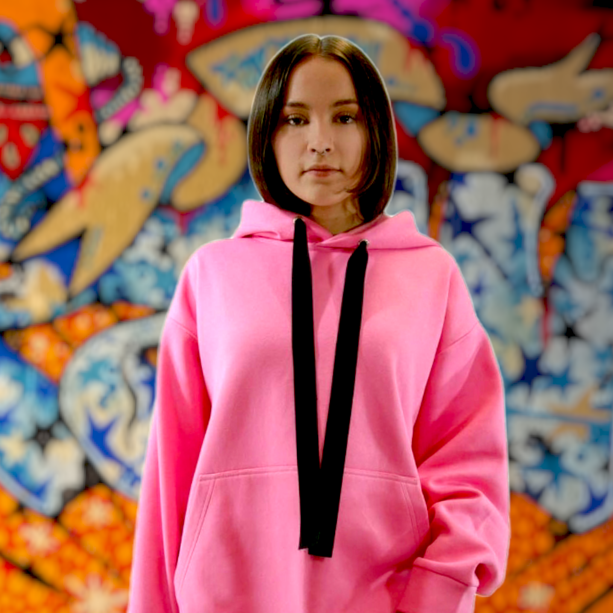 Vadelmanpunainen-pinkki-oversize-hoodie nuoren naisen yllä, taustalla värikäs graffitiseinä. Damaski.
